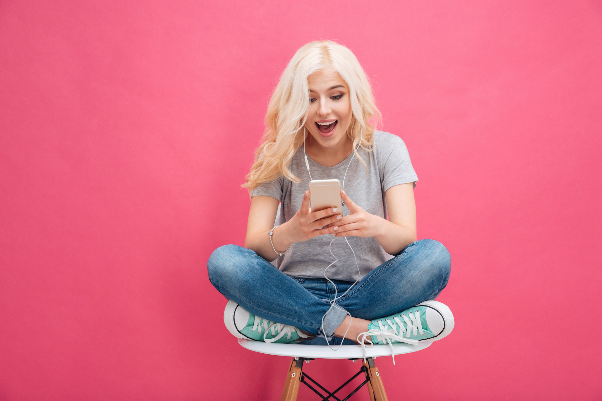 Cheerful young woman using smartphone with headphones over pink background - How We Generated 60,000 Facebook Likes (6 SIMPLE HACKS)